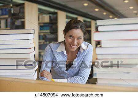 Picture - Portrait of female student between stacks of books. Fotosearch