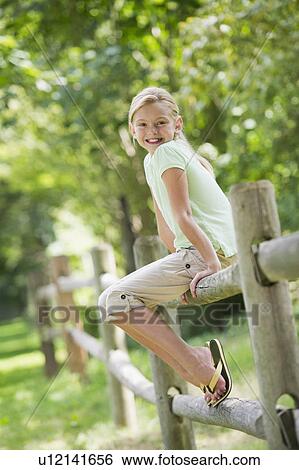 Stock Photograph - Portrait of girl (10-11) sitting on fence. Fotosearch