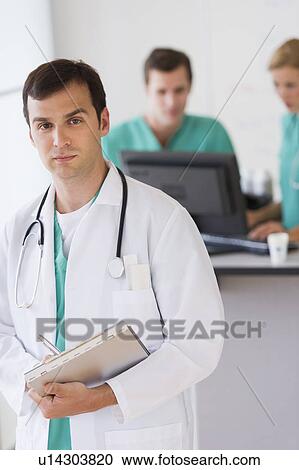 Stock Image - Portrait of male doctor in front of nurse's station. Fotosearch