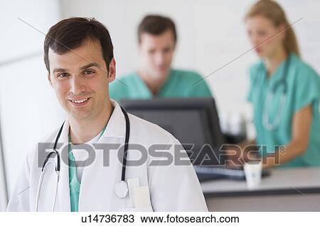 Stock Image - Portrait of male doctor in front of nurse's station. Fotosearch