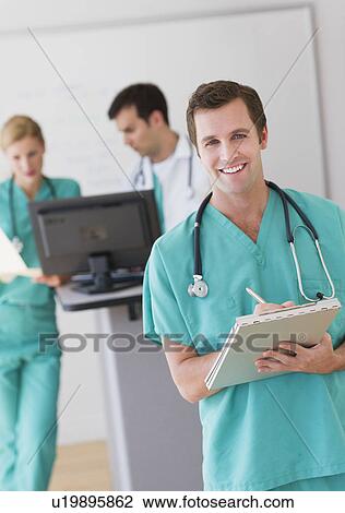 Stock Image - Portrait of male doctor in front of nurse's station. Fotosearch