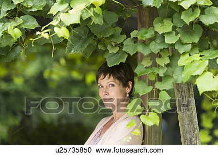 Portrait of mature woman leaning against wooden post overgrown with ivy View Large Photo Image Stock Image - Portrait of mature woman leaning against wooden post overgrown with ivy. Fotosearch
