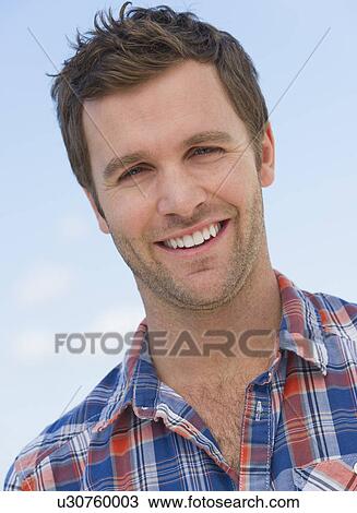 Stock Image - Portrait of mid adult man against blue sky. Fotosearch