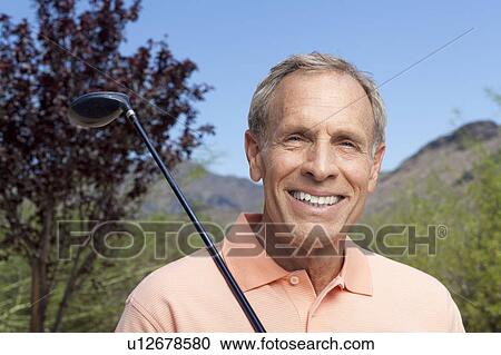 Stock Image - Portrait of senior man holding golf club. Fotosearch