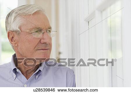 Stock Photograph - Portrait of senior man looking through window. Fotosearch