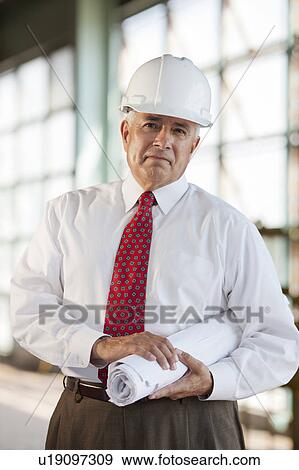 Stock Photo - Portrait of senior man wearing tie and hardhat, holding blueprint. Fotosearch