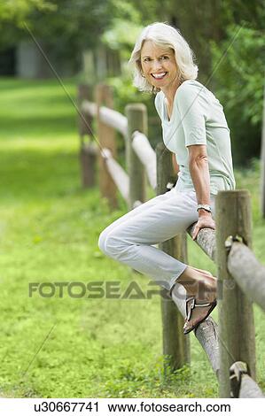 Stock Image - Portrait of senior woman sitting on fence. Fotosearch