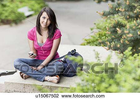 Stock Image - Portrait of woman text-messaging in park. Fotosearch