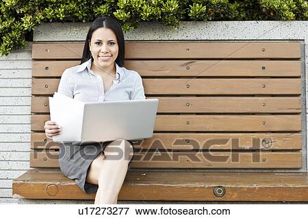 Portrait of young businesswoman sitting on bench using laptop View Large Photo Image Stock Photo - Portrait of young businesswoman sitting on bench using laptop. Fotosearch