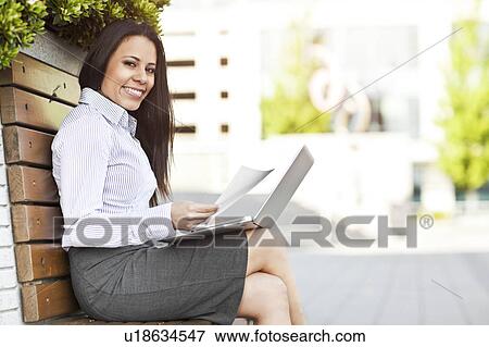 Stock Photo - Portrait of young businesswoman sitting on bench using laptop. Fotosearch