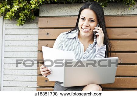 Portrait of young businesswoman sitting on bench using laptop View Large Photo Image Stock Photo - Portrait of young businesswoman sitting on bench using laptop. Fotosearch