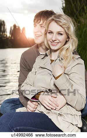Portrait of young couple embracing by lake at sunset View Large Photo Image Stock Photograph - Portrait of young couple embracing by lake at sunset. Fotosearch