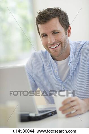 Portrait of young man using laptop and drinking coffee View Large Photo Image Picture - Portrait of young man using laptop and drinking coffee. Fotosearch
