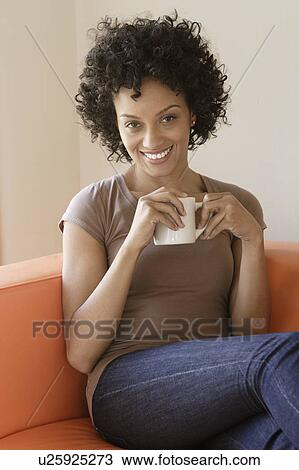 Portrait of young woman sitting on sofa View Large Photo Image Stock Image - Portrait of young woman sitting on sofa. Fotosearch