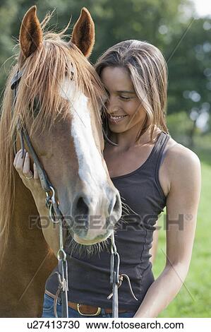 Stock Image - Portrait of young woman with horse in field. Fotosearch