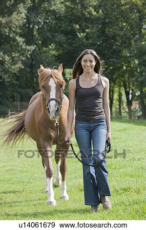 Stock Photo - Portrait of young woman with horse in field. Fotosearch