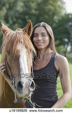 Stock Photograph - Portrait of young woman with horse in field. Fotosearch
