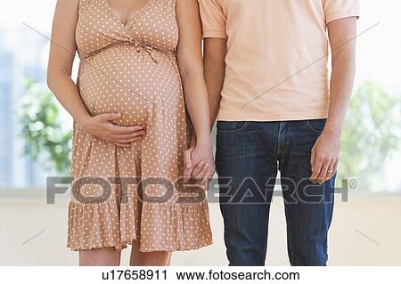 Stock Image - Pregnant woman holding partner's hand. Fotosearch