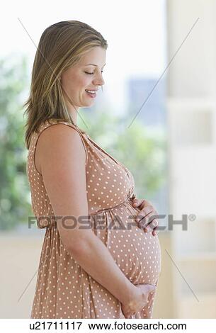 Stock Photo - Pregnant woman looking through window. Fotosearch