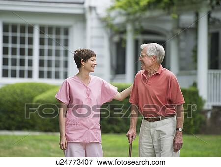 Stock Photo - Senior man and nursing assistant walking in back yard. Fotosearch
