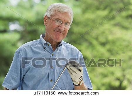Stock Image - Senior man holding golf club, portrait. Fotosearch