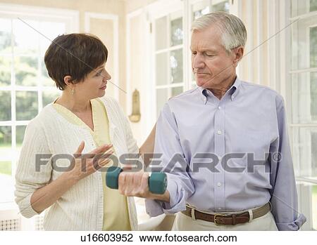 Stock Image - Senior man lifting dumbbell, nurse assisting him. Fotosearch
