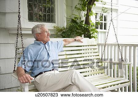 Stock Image - Senior man sitting on porch swing. Fotosearch