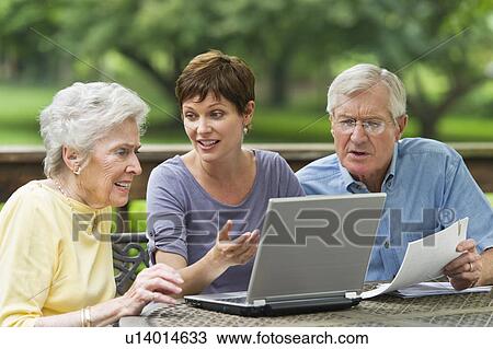 Stock Image - Senior parents and adult daughter using laptop on porch. Fotosearch