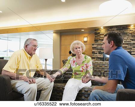 Stock Image - Senior people holding hands in hospital talking to doctor. Fotosearch