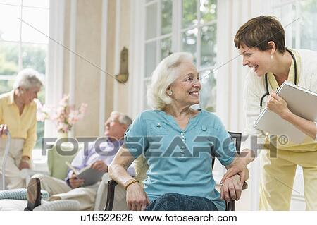 Stock Photograph - Senior woman and nurse talking outside nursing home. Fotosearch
