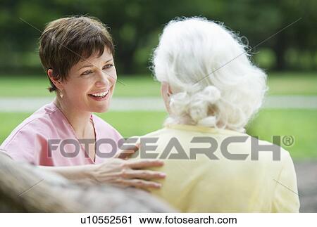Stock Image - Senior woman and nursing assistant relaxing on outdoor sofa. Fotosearch