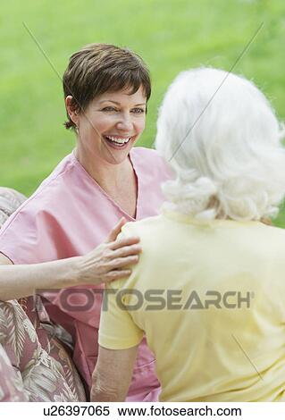 Stock Photography - Senior woman and nursing assistant relaxing on outdoor sofa. Fotosearch