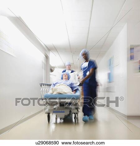 Stock Image - Senior woman being taken to operating room by medical staff. Fotosearch
