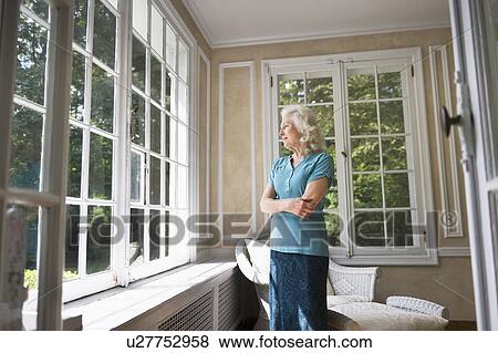 Stock Photo - Senior woman looking through window. Fotosearch
