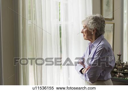Stock Photography - Senior woman looking through window. Fotosearch
