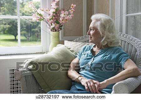 Stock Photo - Senior woman sitting in chair looking through window. Fotosearch