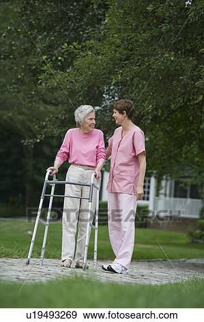 Stock Photo - Senior woman walking with walker with help of nursing assistant. Fotosearch