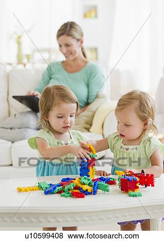 Sisters (2-3) playing in living room, mother in background View Large Photo Image Stock Photo - Sisters (2-3) playing in living room, mother in background. Fotosearch