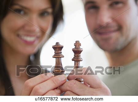 Stock Image - Smiling couple showing chess pieces. Fotosearch