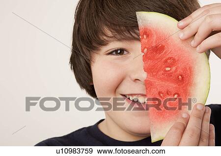 Stock Photo - Studio portrait of boy (10-11) holding slice of watermelon. Fotosearch