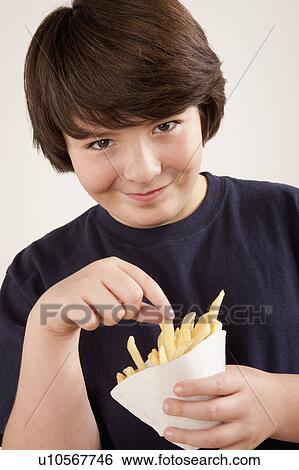 Stock Photograph - Studio portrait of boy (10-11) holding french fries. Fotosearch