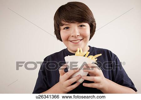 Stock Photograph - Studio portrait of boy (10-11) holding french fries. Fotosearch