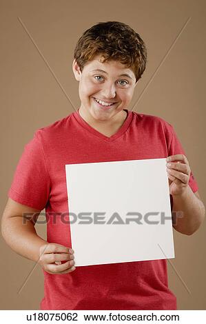 Stock Image - Studio portrait of boy (12-13) holding blank sheet of paper. Fotosearch
