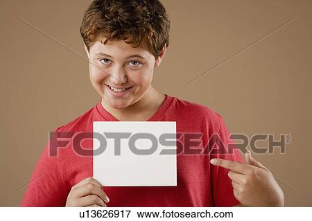 Stock Photo - Studio portrait of boy (12-13) holding blank sheet of paper. Fotosearch