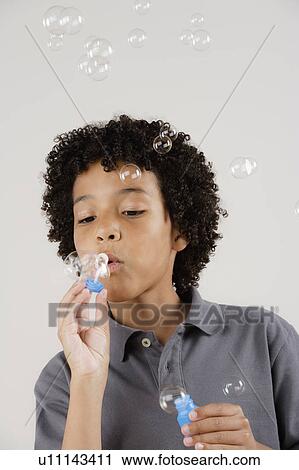 Stock Image - Studio portrait of boy (8-9) blowing bubbles. Fotosearch