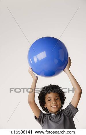 Stock Image - Studio portrait of boy (8-9) holding blue ball. Fotosearch