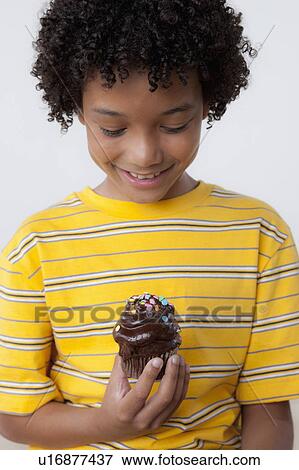 Stock Photo - Studio portrait of boy (8-9) holding muffin. Fotosearch