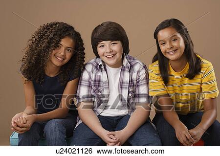 Stock Photograph - Studio portrait of boy and girls (10-11) sitting side by side. Fotosearch