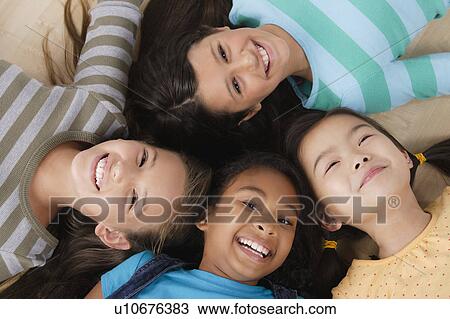 Stock Image - Studio portrait of four girls (8-9) lying on floor. Fotosearch