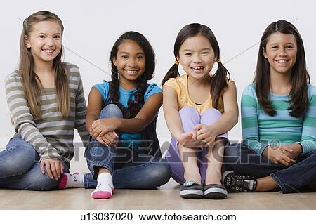 Stock Image - Studio portrait of four girls (8-9) sitting side by side. Fotosearch